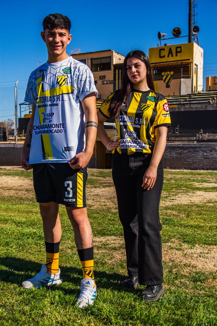 Two young adults outdoors wearing soccer team jerseys, symbolizing sports passion.