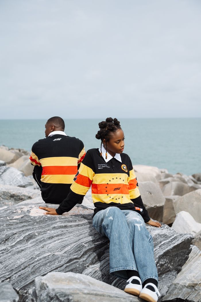 A young couple sits on rocks by the ocean in Lagos, Nigeria, showcasing casual fashion against a serene backdrop.