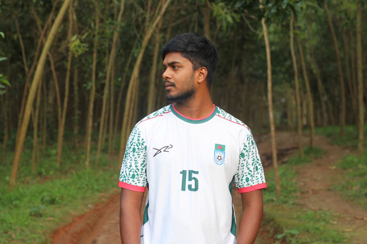 Young man wearing a sports jersey on a forest path, looking sideways.
