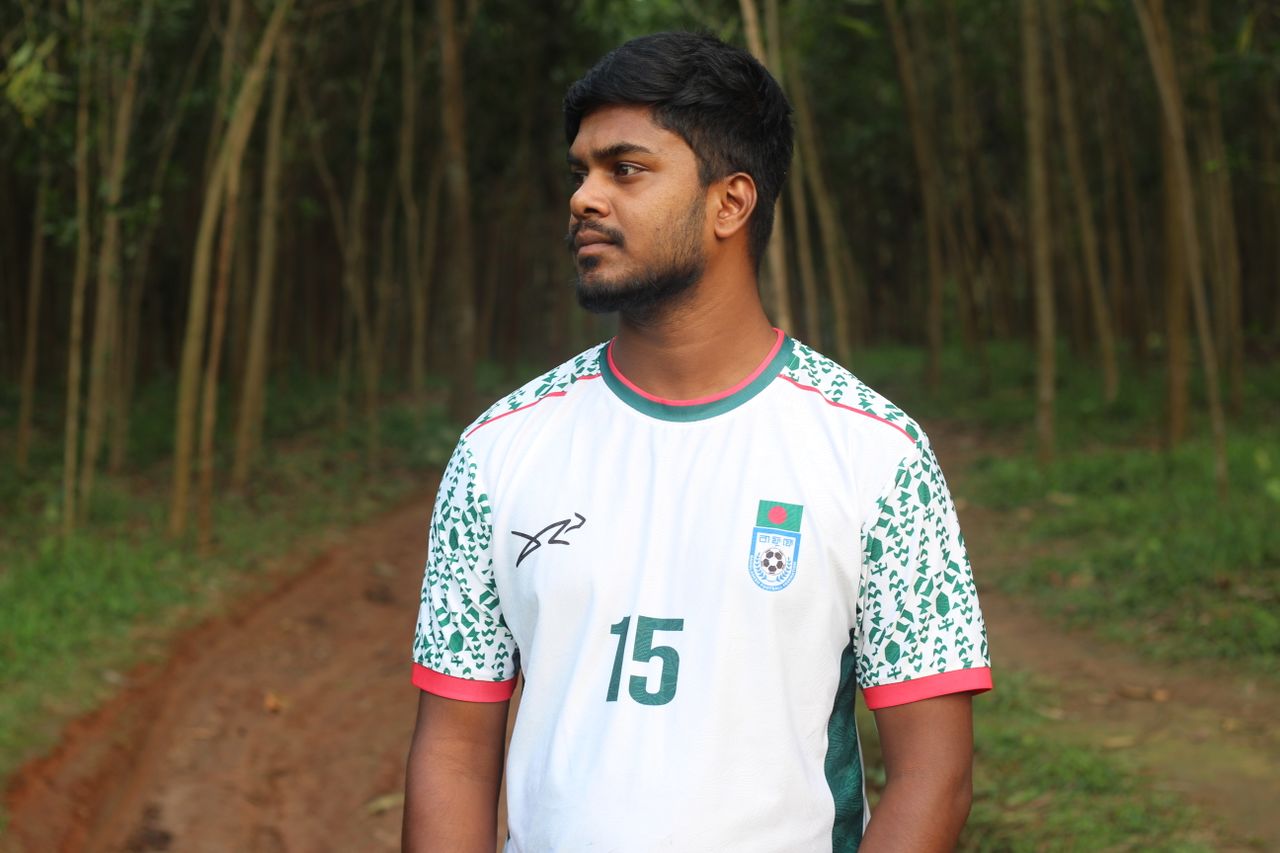 A young man wearing a football jersey standing in a forest path.